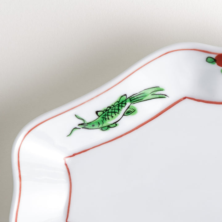 An irregularly shaped porcelain dish featuring hand-painted designs of fish and plants.