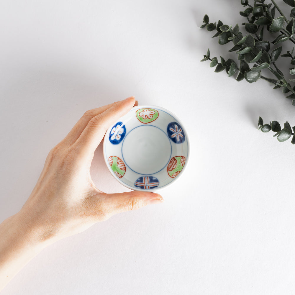 A small raised sauce dish adorned with traditional Japanese motifs, including floral and geometric patterns in red, blue, and green.