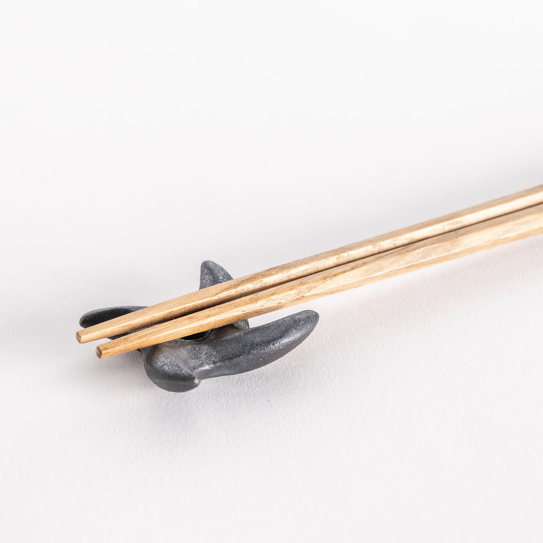 Close-up of a ninja star-shaped chopstick rest in metallic black, holding a pair of chopsticks securely in the center groove.