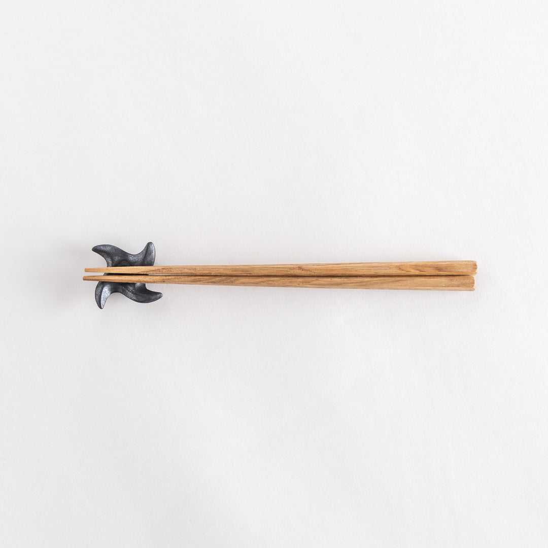 Top-down view of a ninja star-shaped chopstick rest in metallic black, holding chopsticks, with its geometric design clearly visible.