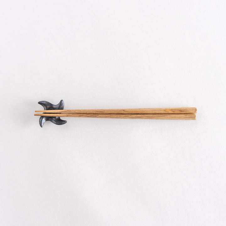 Top-down view of a ninja star-shaped chopstick rest in metallic black, holding chopsticks, with its geometric design clearly visible.