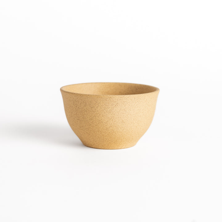 Beige ceramic teacup photographed from the side, highlighting its elegant curved silhouette and textured surface.