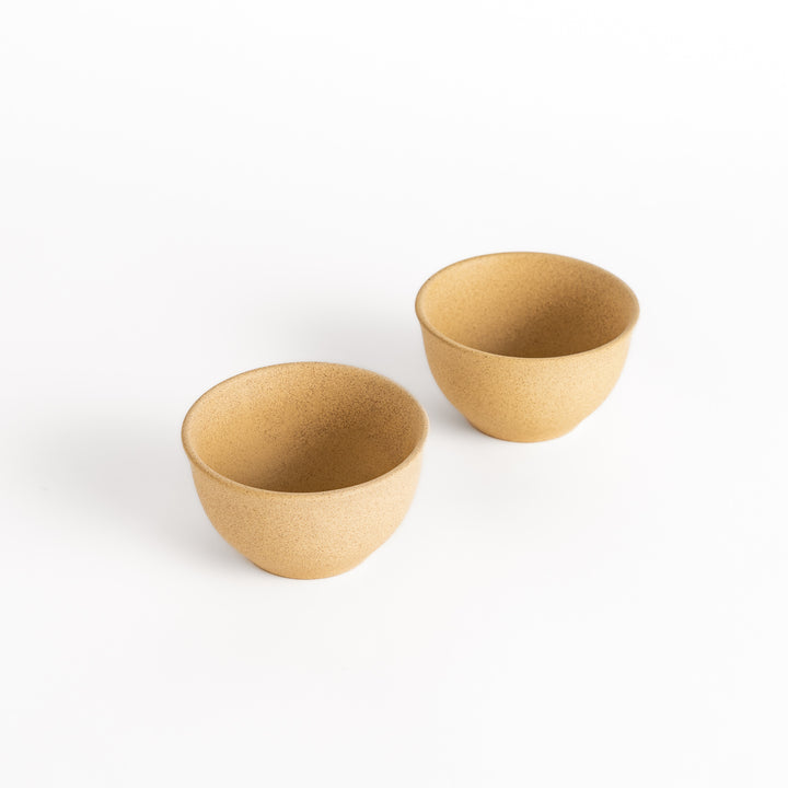 Two beige ceramic teacups with a textured surface, displayed side by side, part of a beautifully crafted two-piece set.