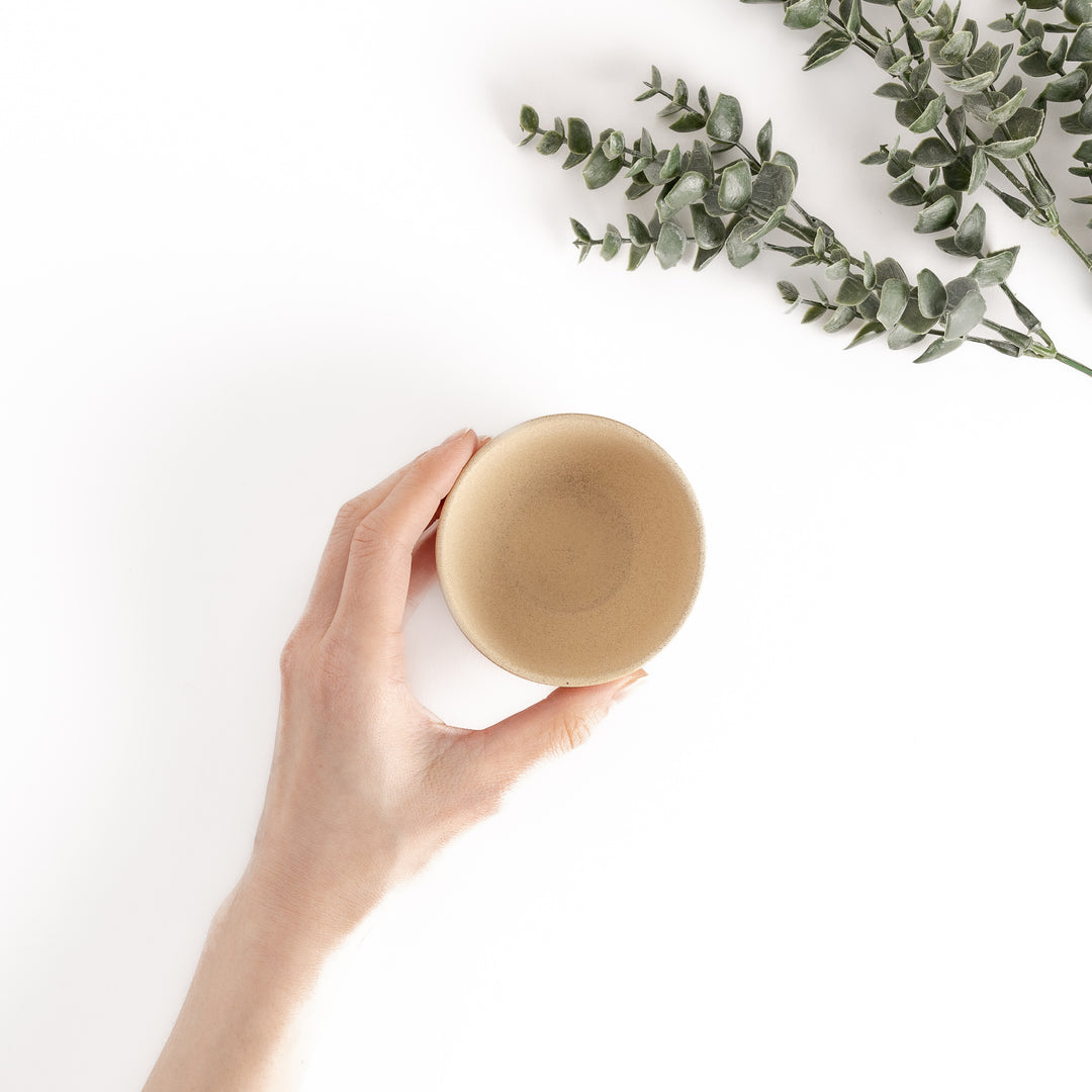 Top-down view of a beige teacup with a hand gently holding it, showcasing its rounded rim and smooth interior.