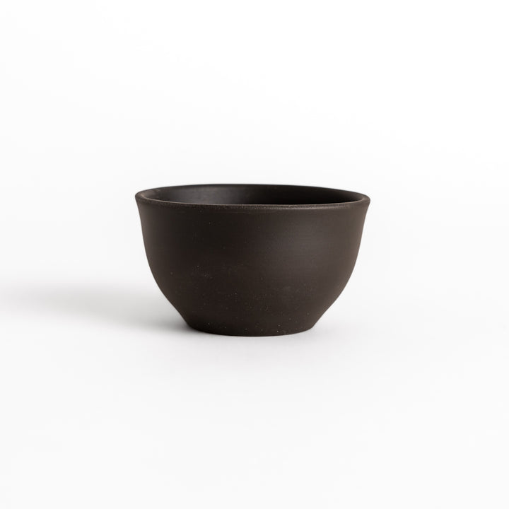 Black ceramic teacup photographed from the side, highlighting its elegant curved silhouette and matte finish.