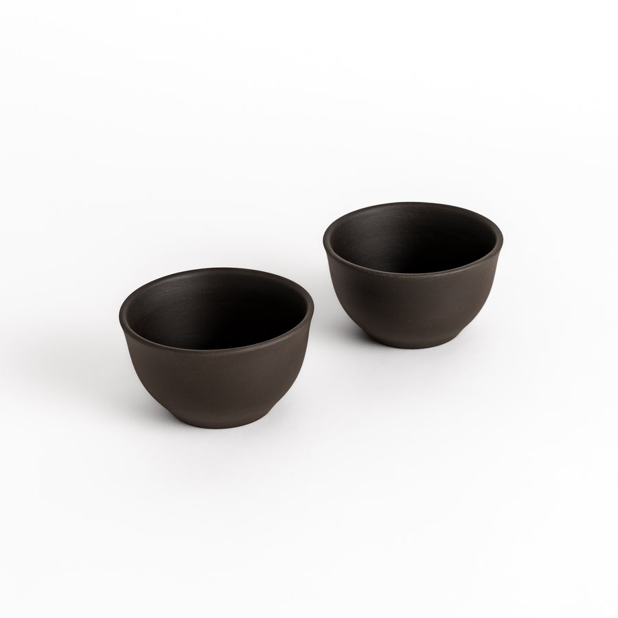 Two black ceramic teacups with a matte finish, displayed side by side, part of a beautifully crafted two-piece set.