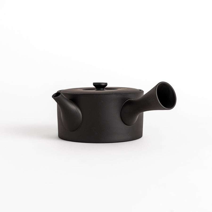 Minimalist black teapot with a horizontal spout and handle, crafted from textured ceramic, perfect for a refined tea experience.