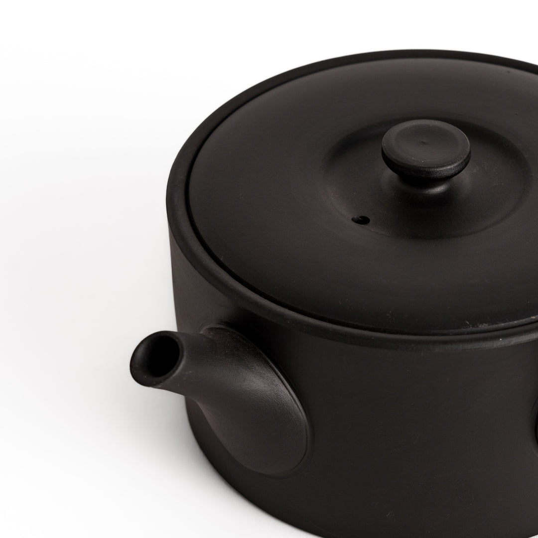 Close-up of the black teapot’s spout and textured surface, emphasizing its fine craftsmanship and detail.