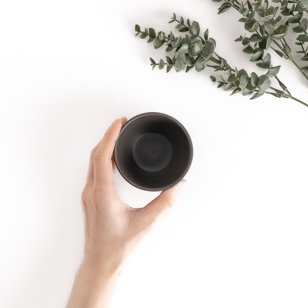 Top-down view of a black teacup with a hand gently holding it, showcasing its rounded rim and smooth interior.