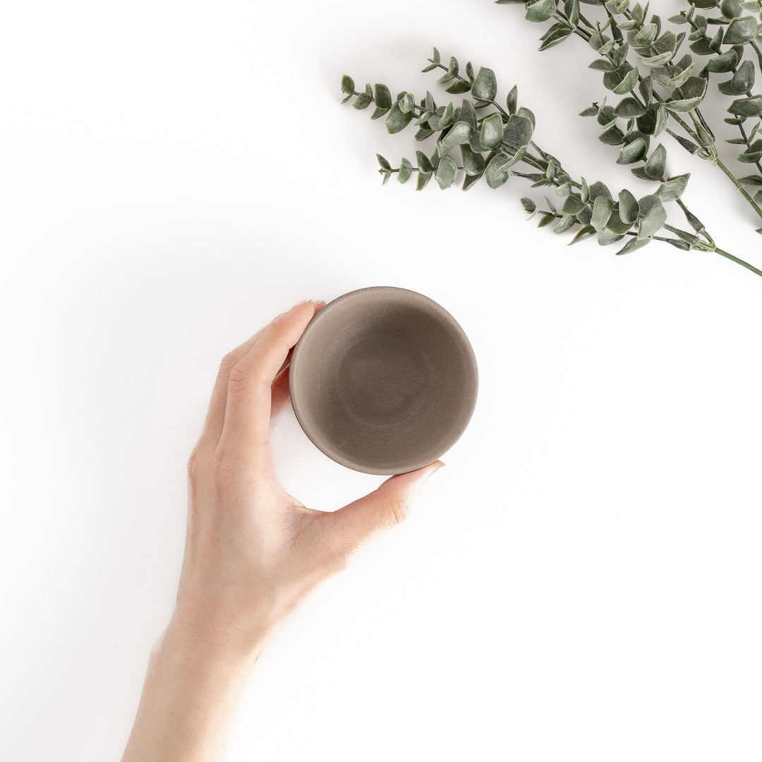 Top-down view of a gray teacup with a hand gently holding it, showcasing its rounded rim and smooth interior.