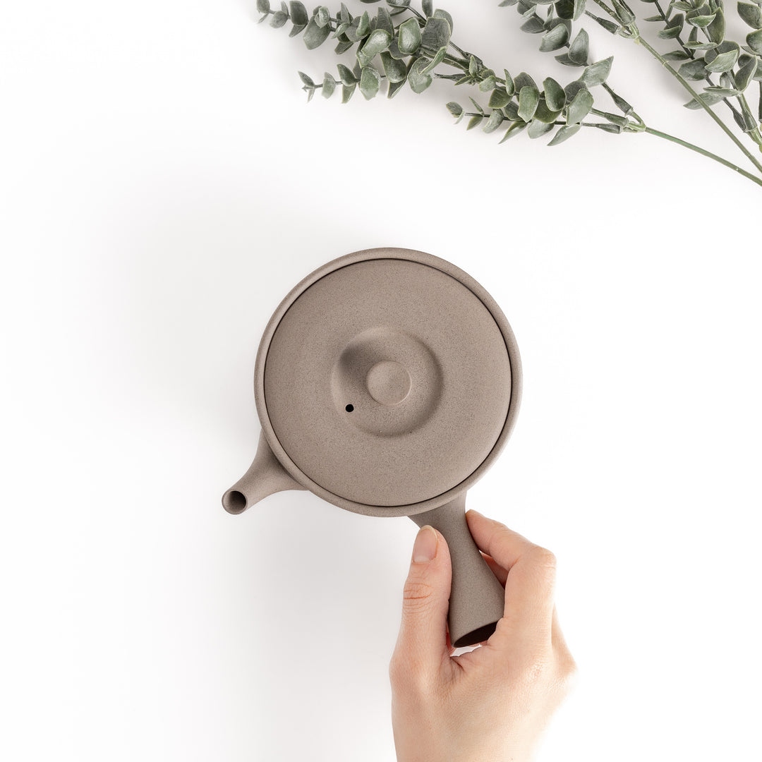 Top-down view of the gray teapot with a hand on the handle, showcasing its ergonomic design and practical proportions.