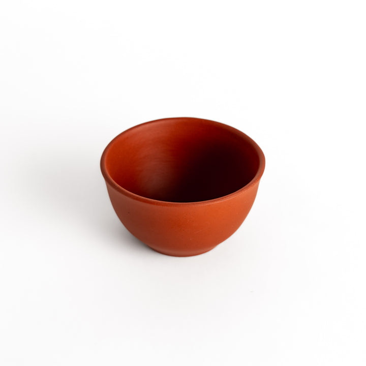 Slightly angled view of a red teacup, focusing on its seamless curves and deep interior.