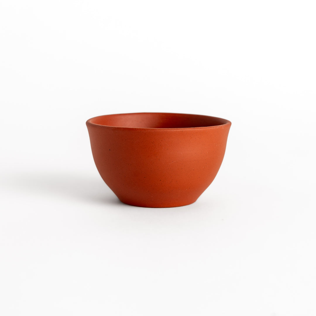 Side view of a single red teacup, highlighting its smooth surface and elegant rounded shape.