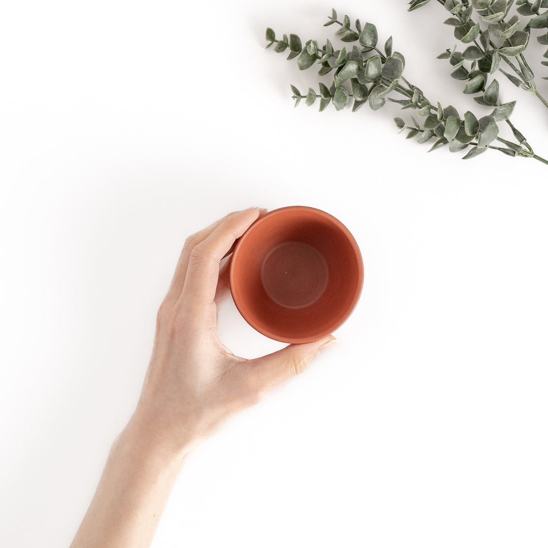 A red teacup viewed from above with a hand gently holding it, showcasing its ergonomic design.