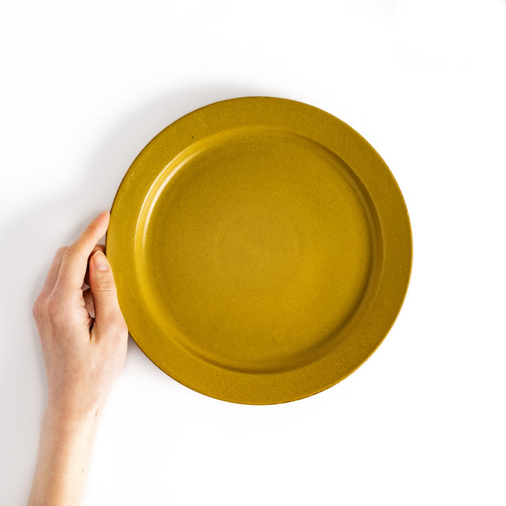 Hand holding a yellow ceramic dinner plate with a glossy finish, adding a cheerful and warm vibe to the setting.