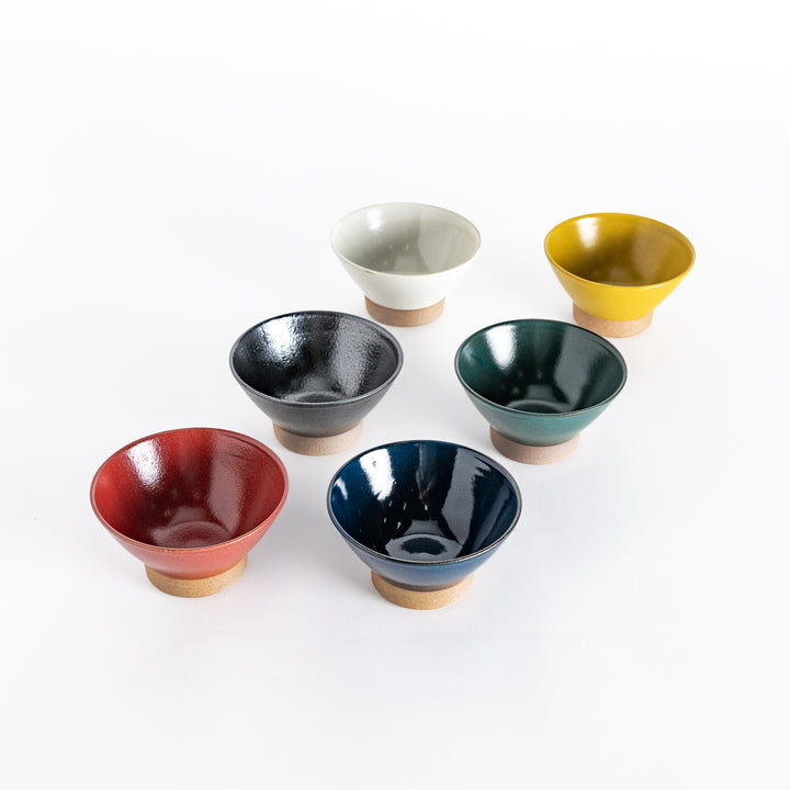 Six ceramic rice bowls in red, black, white, green, blue, and yellow, arranged in a semi-circle. Each bowl has a glossy finish and a neutral-toned base.