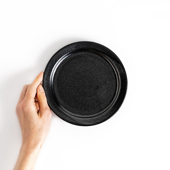 Hand holding a black salad plate, showcasing its size and versatile design ideal for salads and sides.