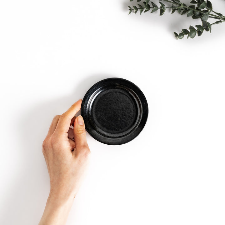 Hand-held black ceramic sauce dish showcasing its sleek glossy surface and compact size, perfect for everyday use.