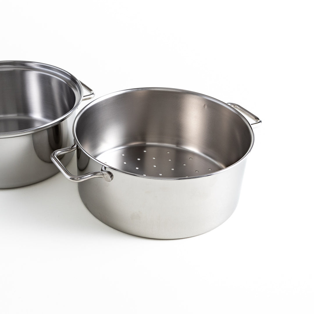 Stainless steel steamer section with perforated base, perfect for even steam distribution, placed alongside its solid base section.