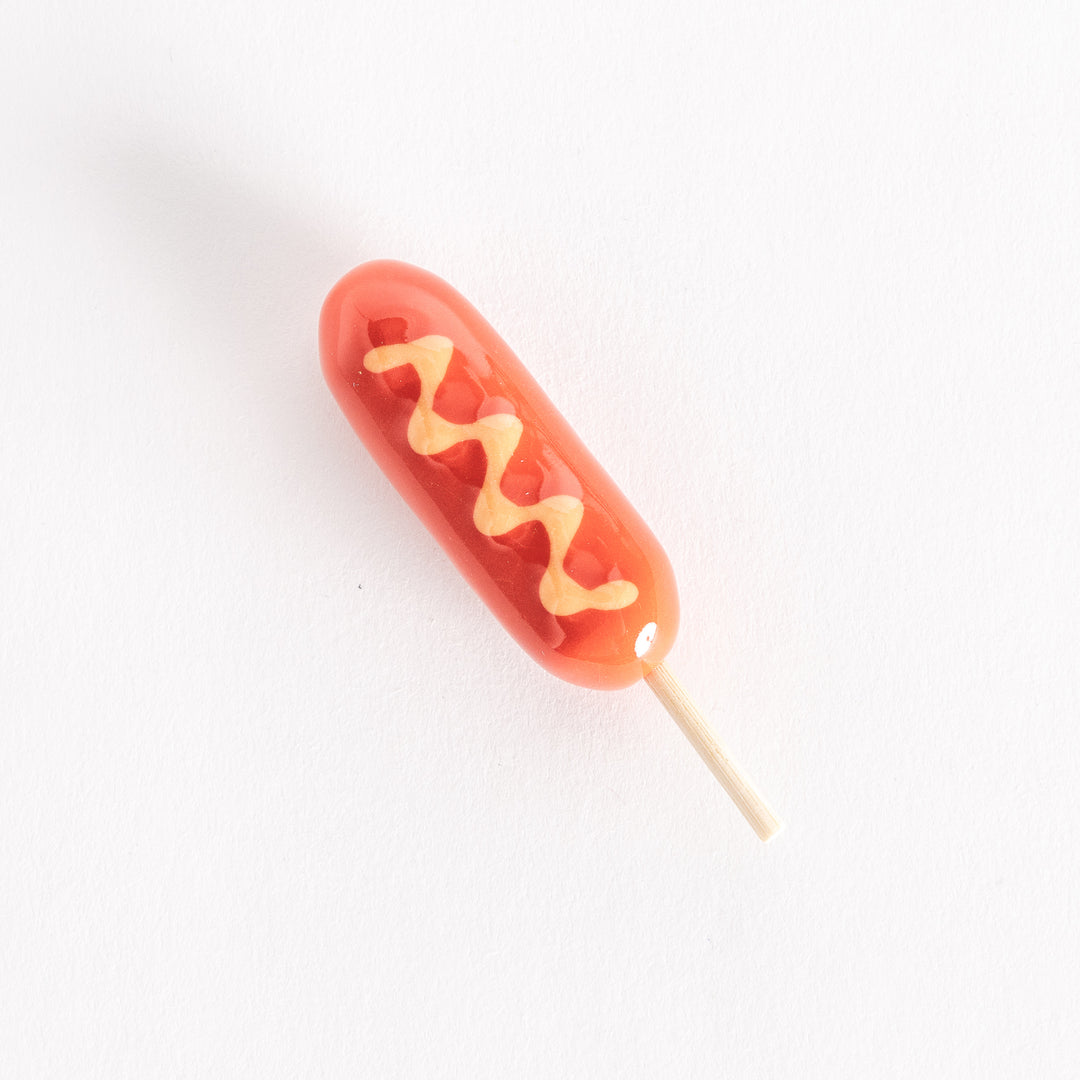 Corn dog-shaped chopsticks rest with a glossy red finish, yellow mustard design, and a wooden stick.