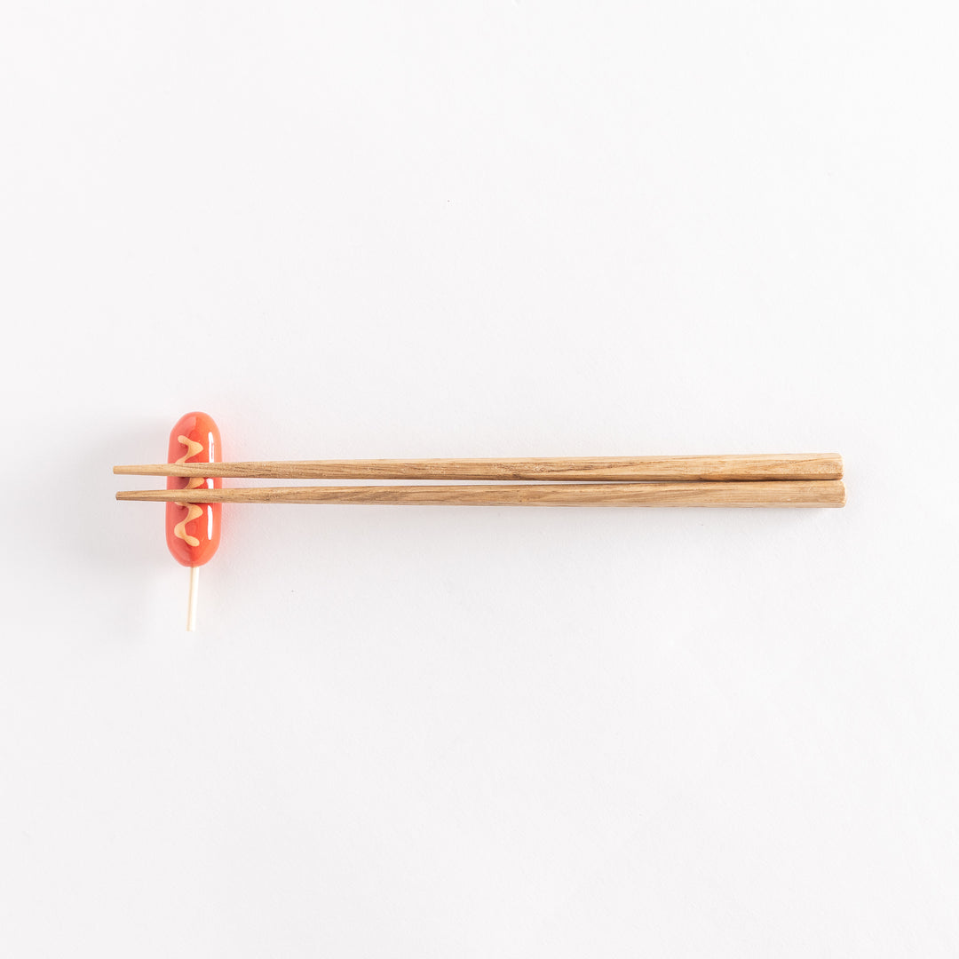 Full view of a corn dog chopsticks rest with wooden chopsticks resting on top.