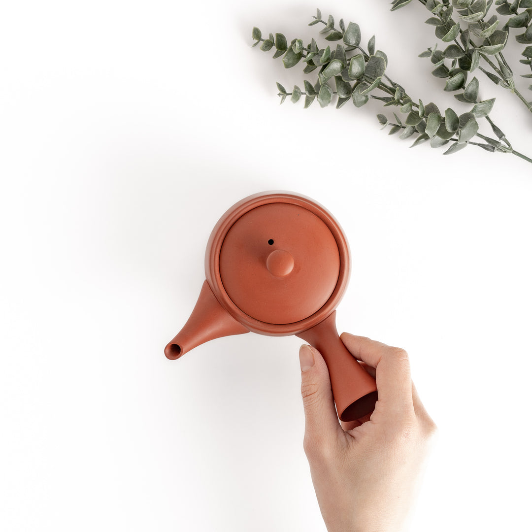 Top-down view of the teapot with a hand holding its handle, showcasing its ergonomic and balanced design.