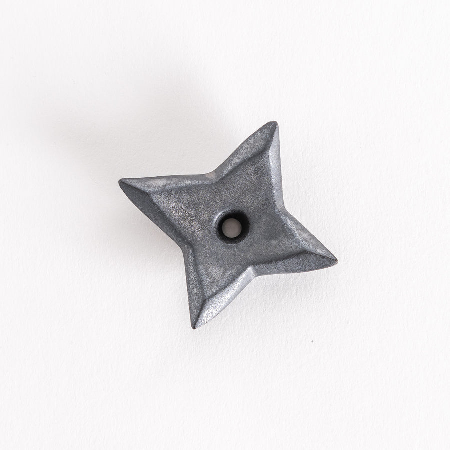 Close-up of a black ninja star-shaped chopstick rest with a pointed design and a small hole at the center, capturing its geometric, angular appearance.