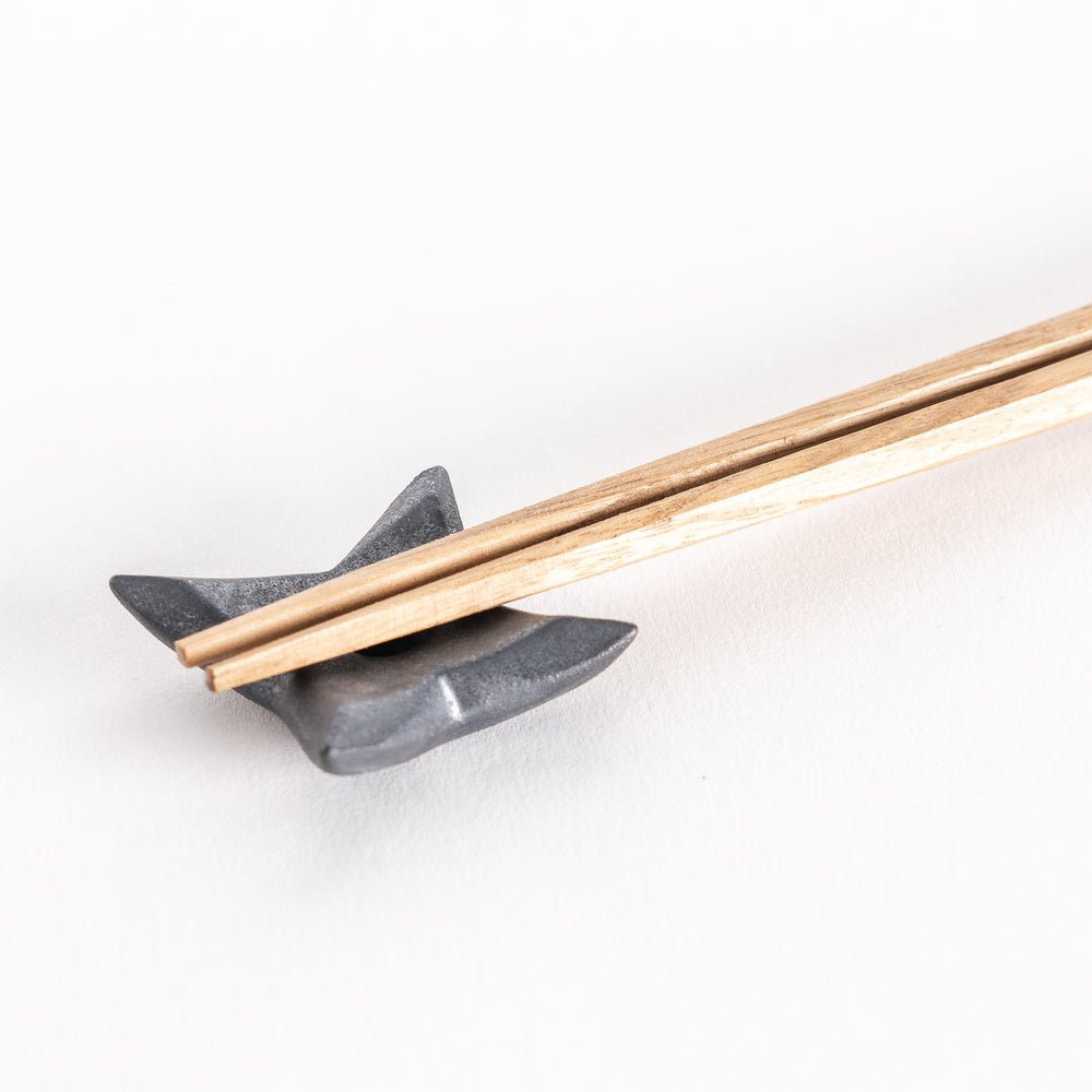 Close-up of a ninja star-shaped chopstick rest in metallic black, holding a pair of chopsticks securely in the center groove.