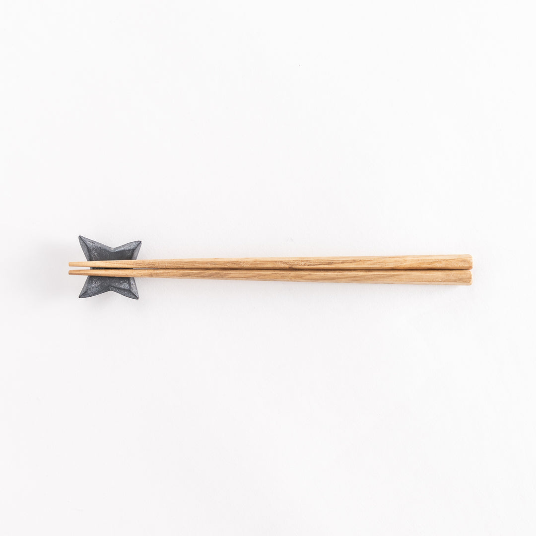 Top-down view of a ninja star-shaped chopstick rest in metallic black, holding chopsticks, with its geometric design clearly visible.