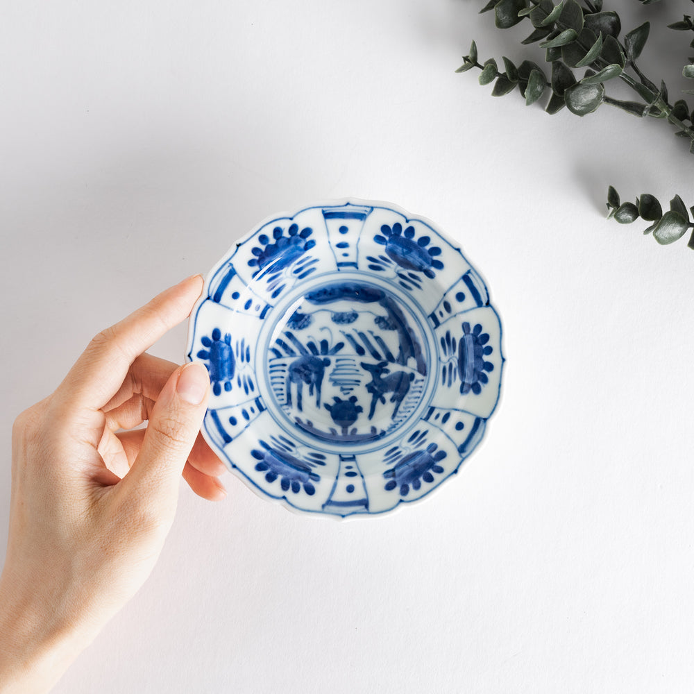 A dessert bowl with a scalloped edge, decorated in blue with pastoral scenes of deer and landscape motifs.