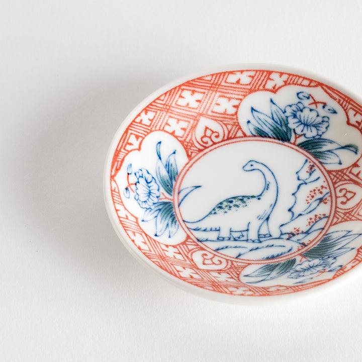 A set of four small, decorative porcelain plates in a gift box, each plate featuring a different dinosaur design in blue and red.