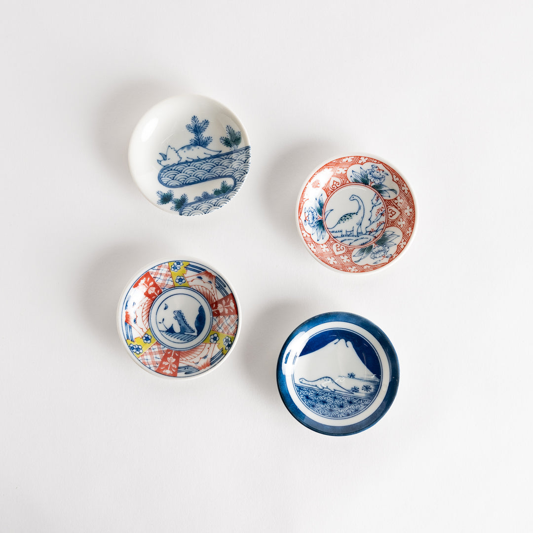 A set of four small, decorative porcelain plates in a gift box, each plate featuring a different dinosaur design in blue and red.