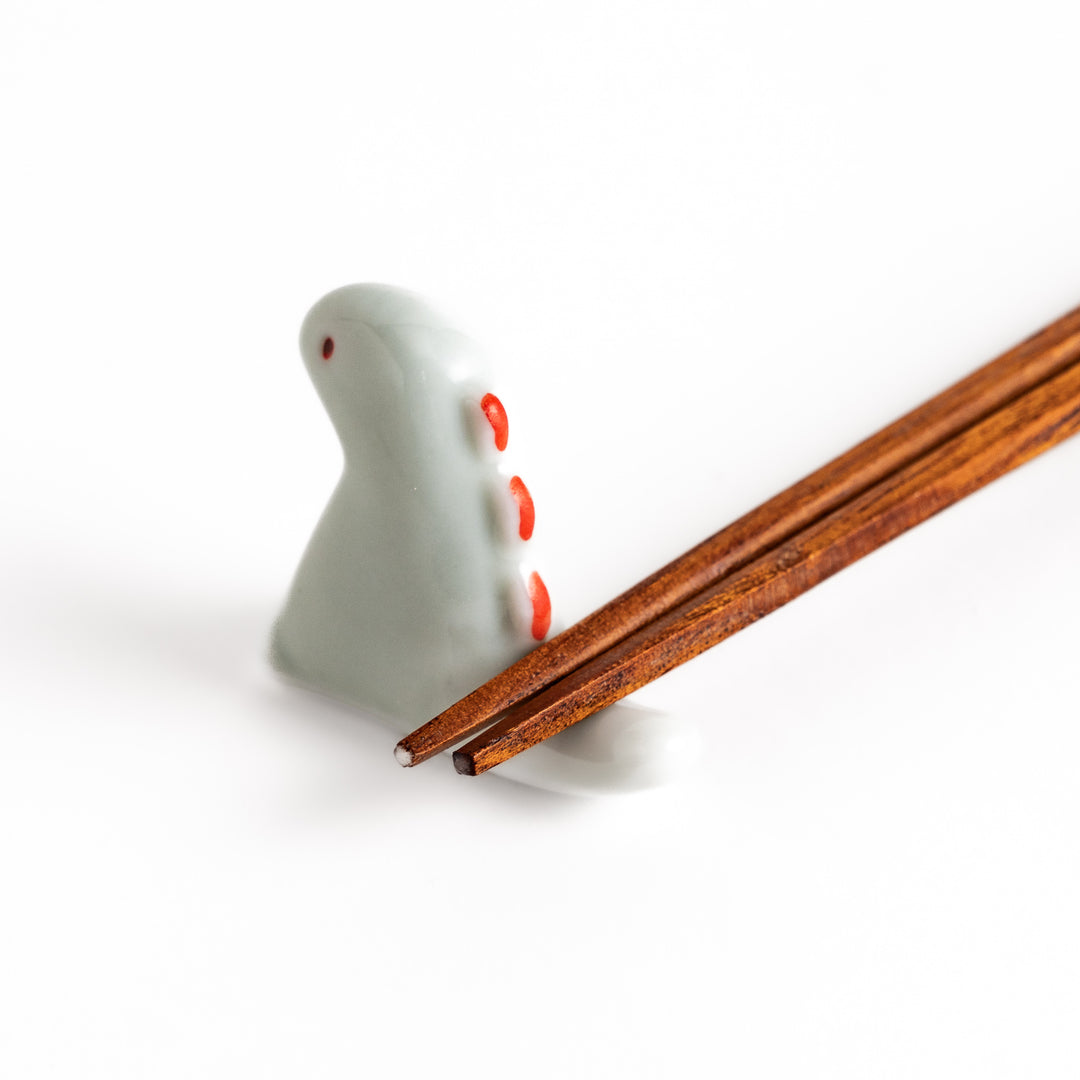 Wooden chopsticks resting on a whimsical white ceramic chopstick rest shaped like a cute dinosaur.