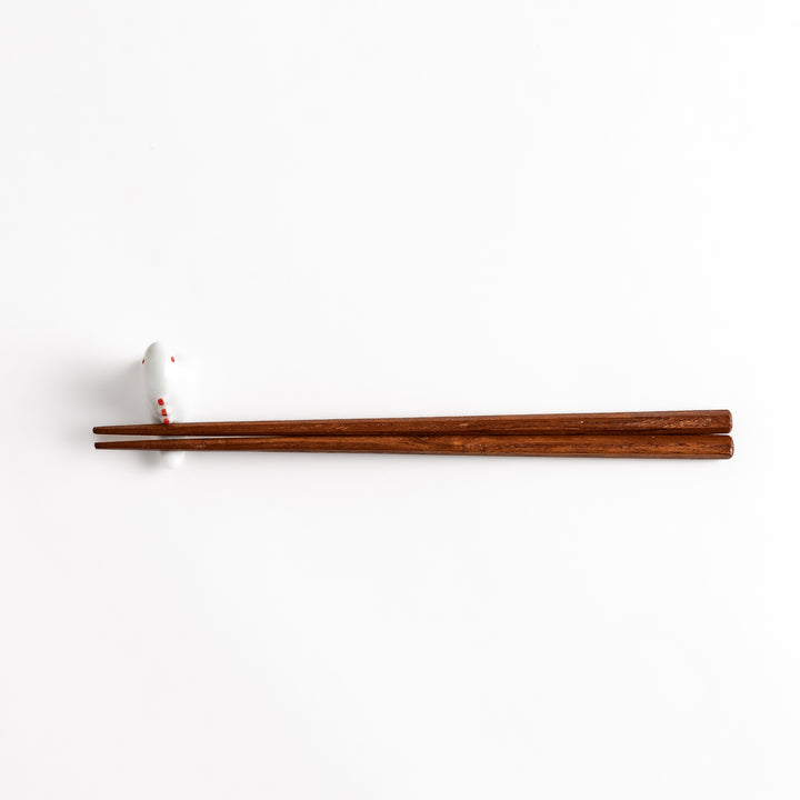 Wooden chopsticks resting on a whimsical white ceramic chopstick rest shaped like a cute dinosaur.