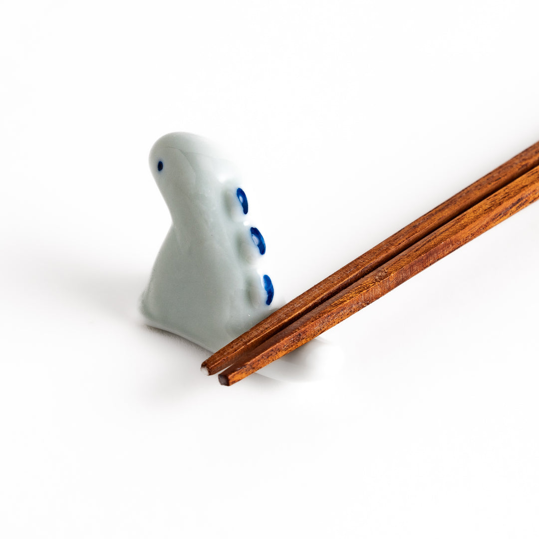 Wooden chopsticks resting on a whimsical white ceramic chopstick rest shaped like a cute dinosaur.