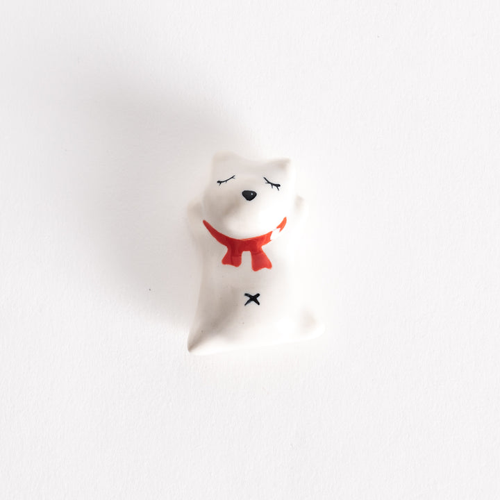 A ceramic chopstick rest shaped like a sleeping dog, featuring a red scarf and closed eyes on a white body.