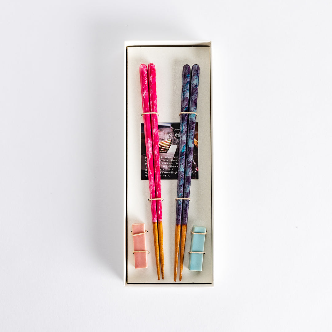 Two pairs of chopsticks in the box, one in pink with swirls and the other in a dark color with blue accents, tied together with a band.