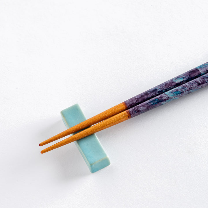 Close-up of dark blue chopstick tips with a subtle sparkle, resting on a blue ceramic holder.