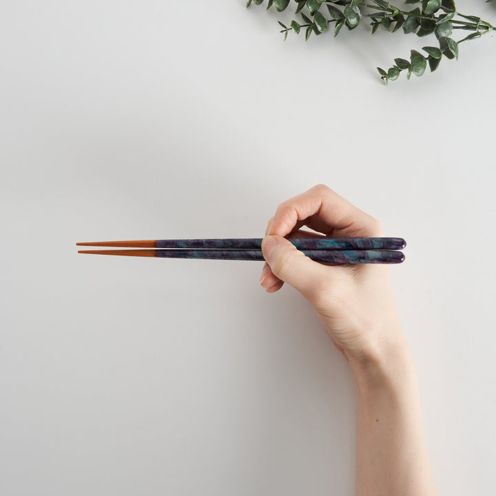 Dark blue chopsticks being held by a hand, demonstrating size.