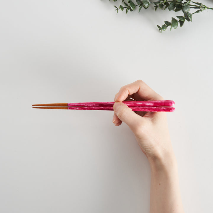 Pink chopsticks being held by a hand, demonstrating size.