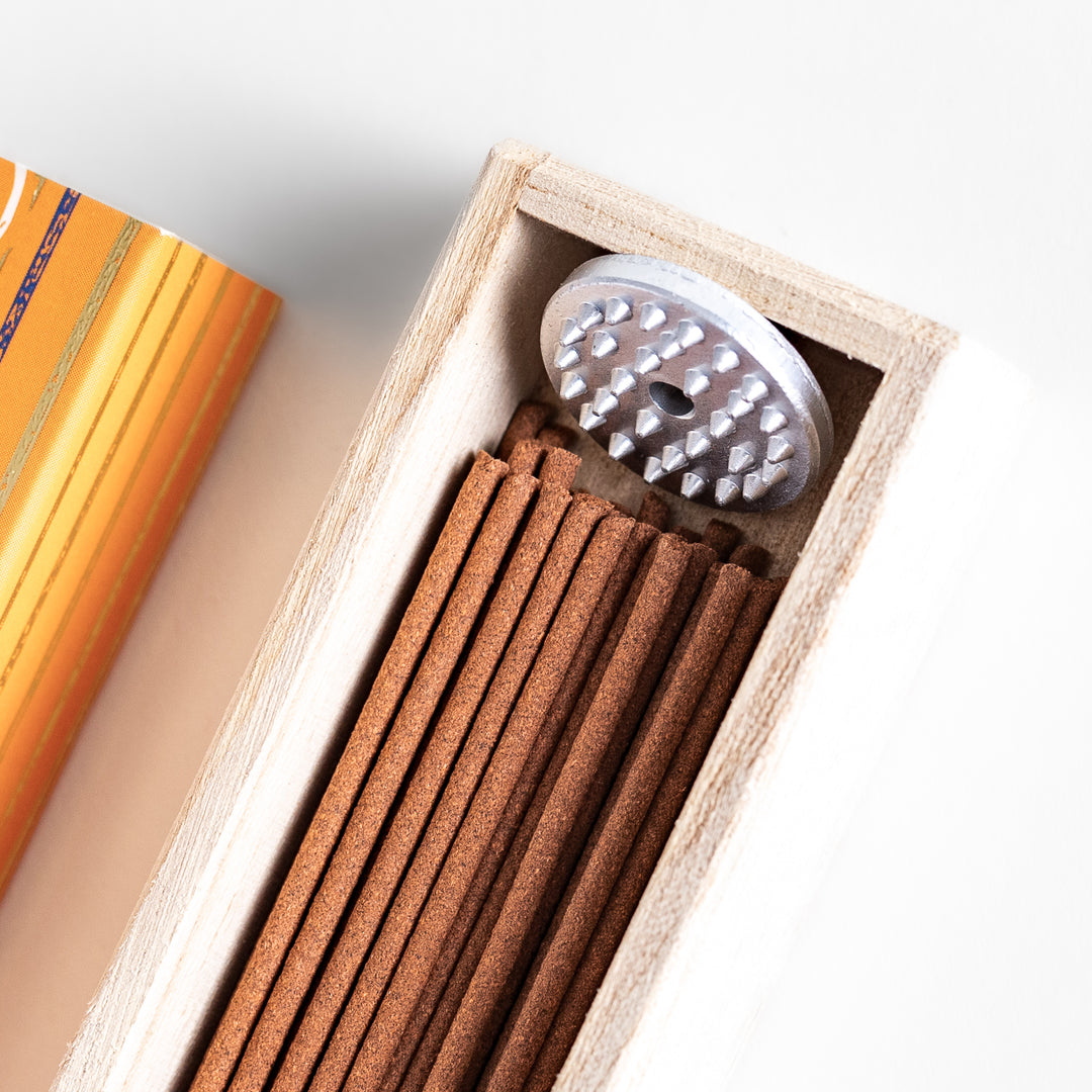 Earthy Patchouli Incense in a light wooden box with warm brown sticks, elegantly packaged in an orange design featuring white circular patterns, evoking a rich and grounding aroma.