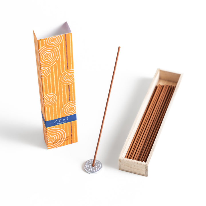 Earthy Patchouli Incense in a light wooden box with warm brown sticks, elegantly packaged in an orange design featuring white circular patterns, evoking a rich and grounding aroma.