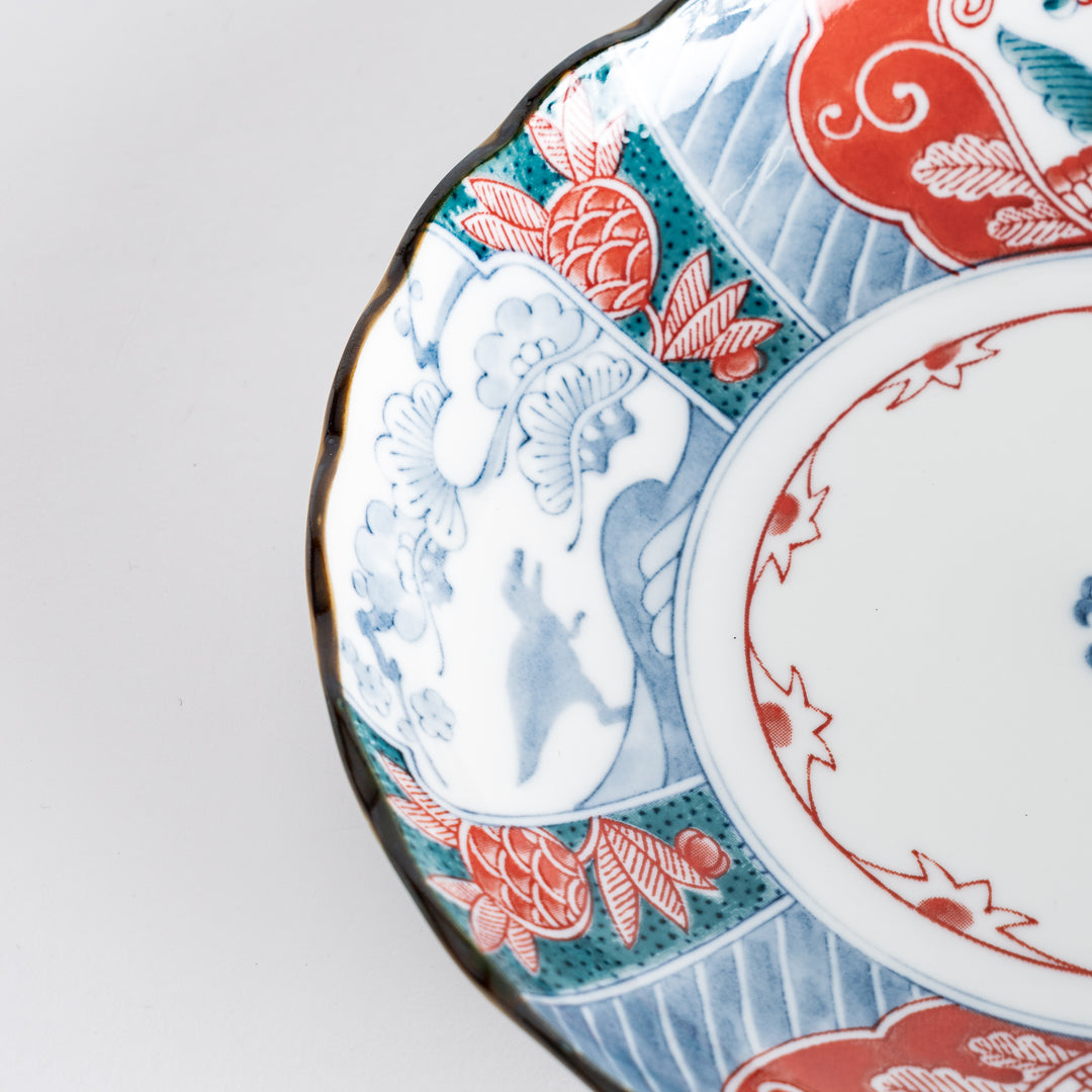 Close-up of the decorative plate's edge, revealing intricate patterns in red, blue, and green against the white base.