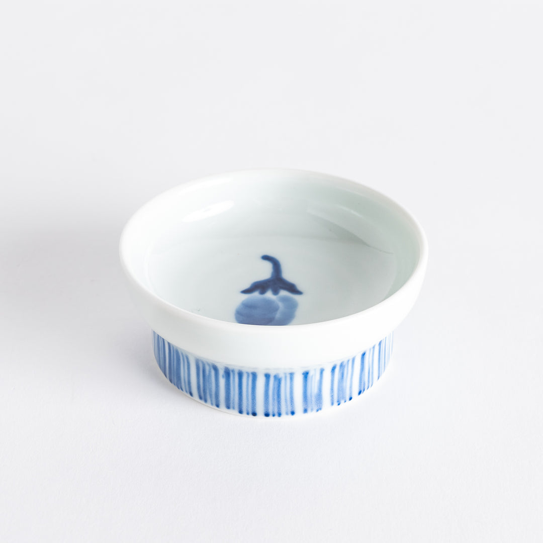 A small raised sauce dish featuring a minimalist blue eggplant design on the inside and vertical blue lines along the outer edge.