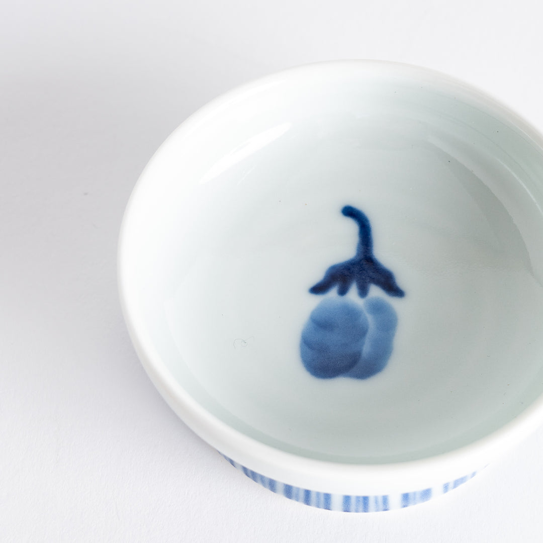 A small raised sauce dish featuring a minimalist blue eggplant design on the inside and vertical blue lines along the outer edge.