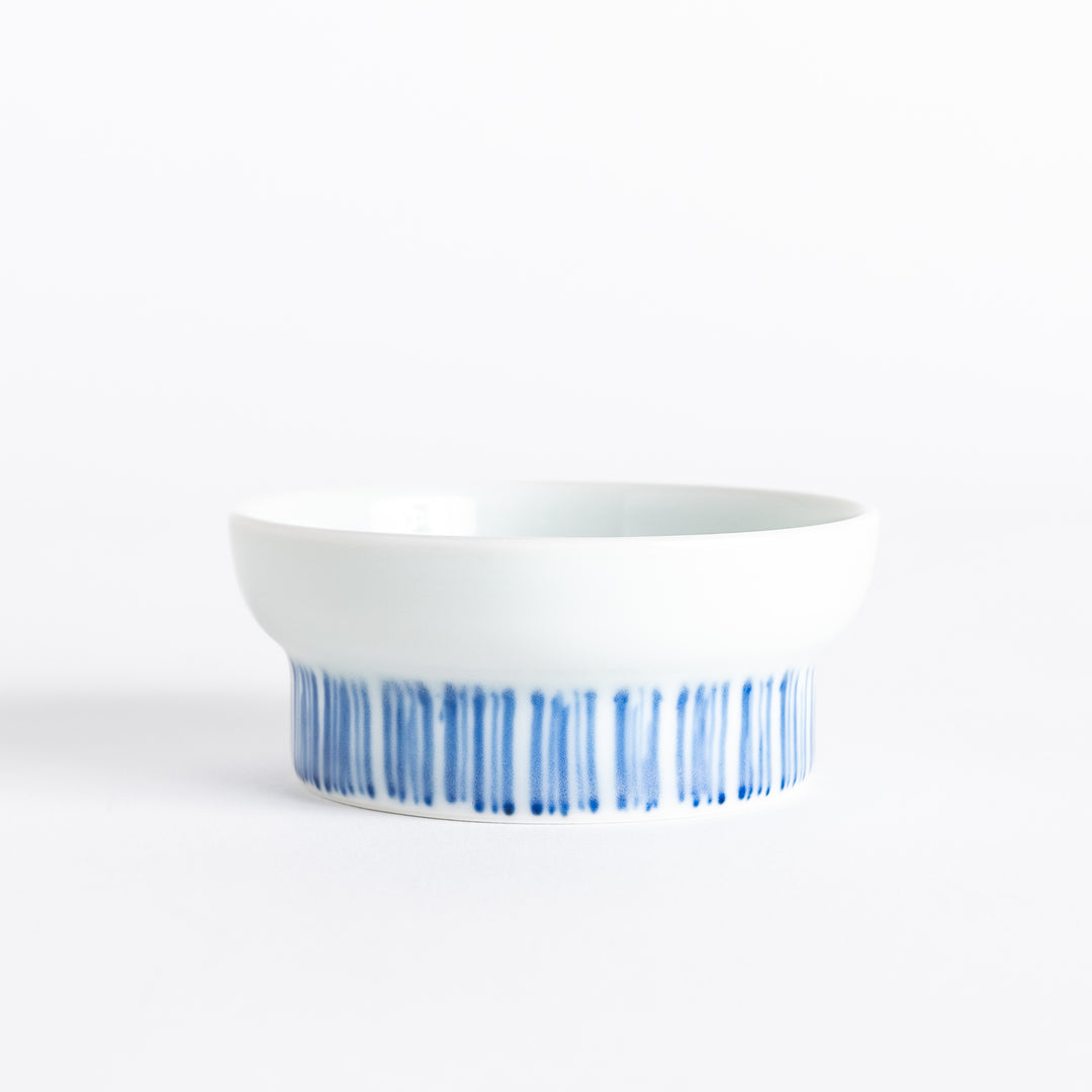 A small raised sauce dish featuring a minimalist blue eggplant design on the inside and vertical blue lines along the outer edge.