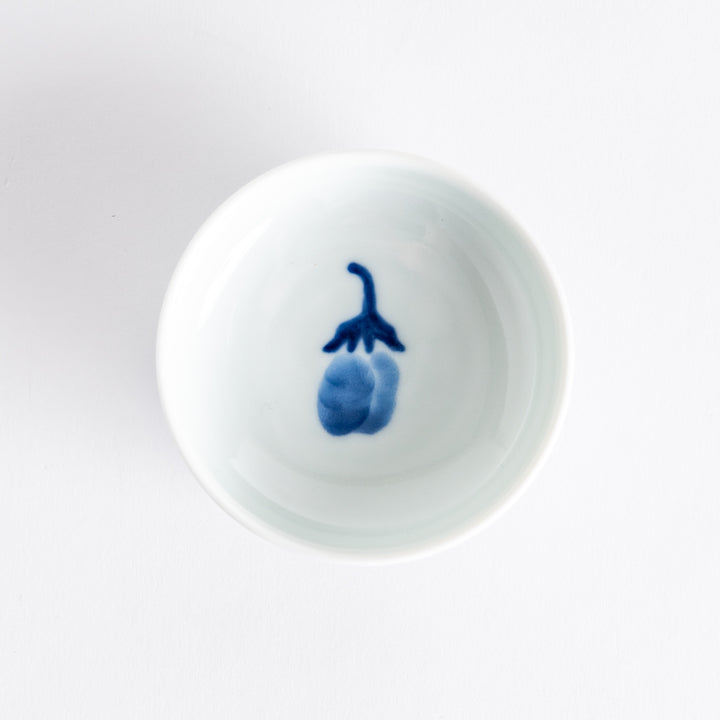 A small raised sauce dish featuring a minimalist blue eggplant design on the inside and vertical blue lines along the outer edge.