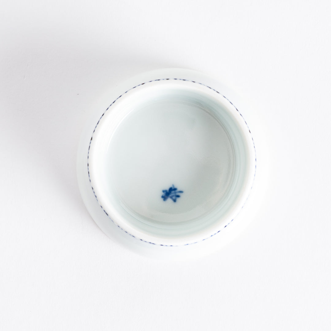 A small raised sauce dish featuring a minimalist blue eggplant design on the inside and vertical blue lines along the outer edge.