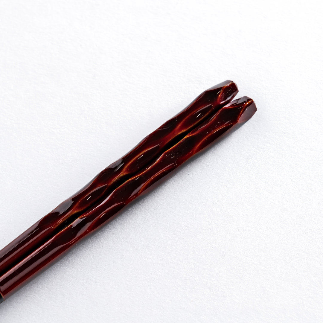 Close-up of the handle of the Ember color chopstick, displaying the intricate carving and rich, warm hues.