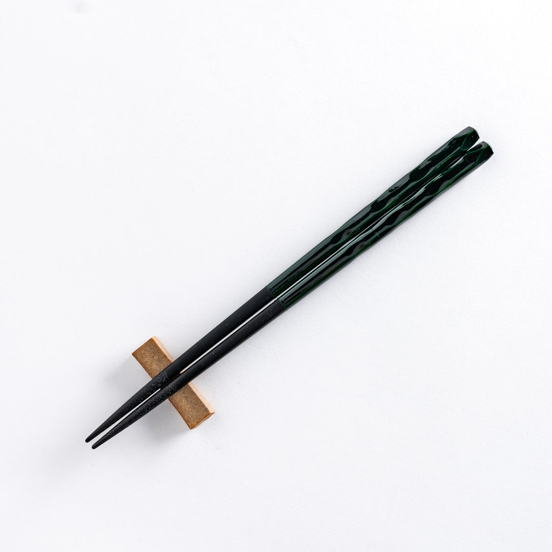 Forest color chopstick resting on a chopstick rest, showcasing its deep green tone and detailed carving.